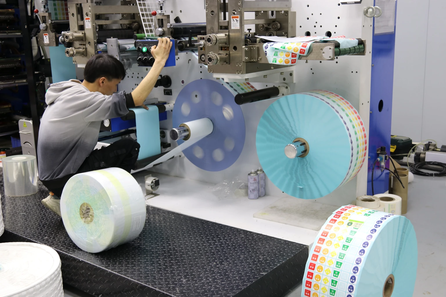 Operator beside a cyan-backed printed label web on production equipment