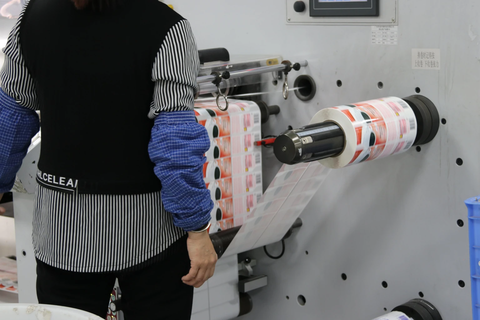 Operator beside a wide roll of printed labels and its continuous web