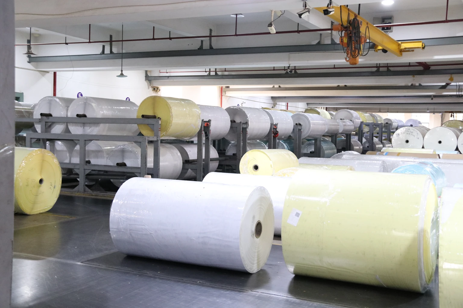 Large wrapped white and pale-coloured paper stock rolls in storage