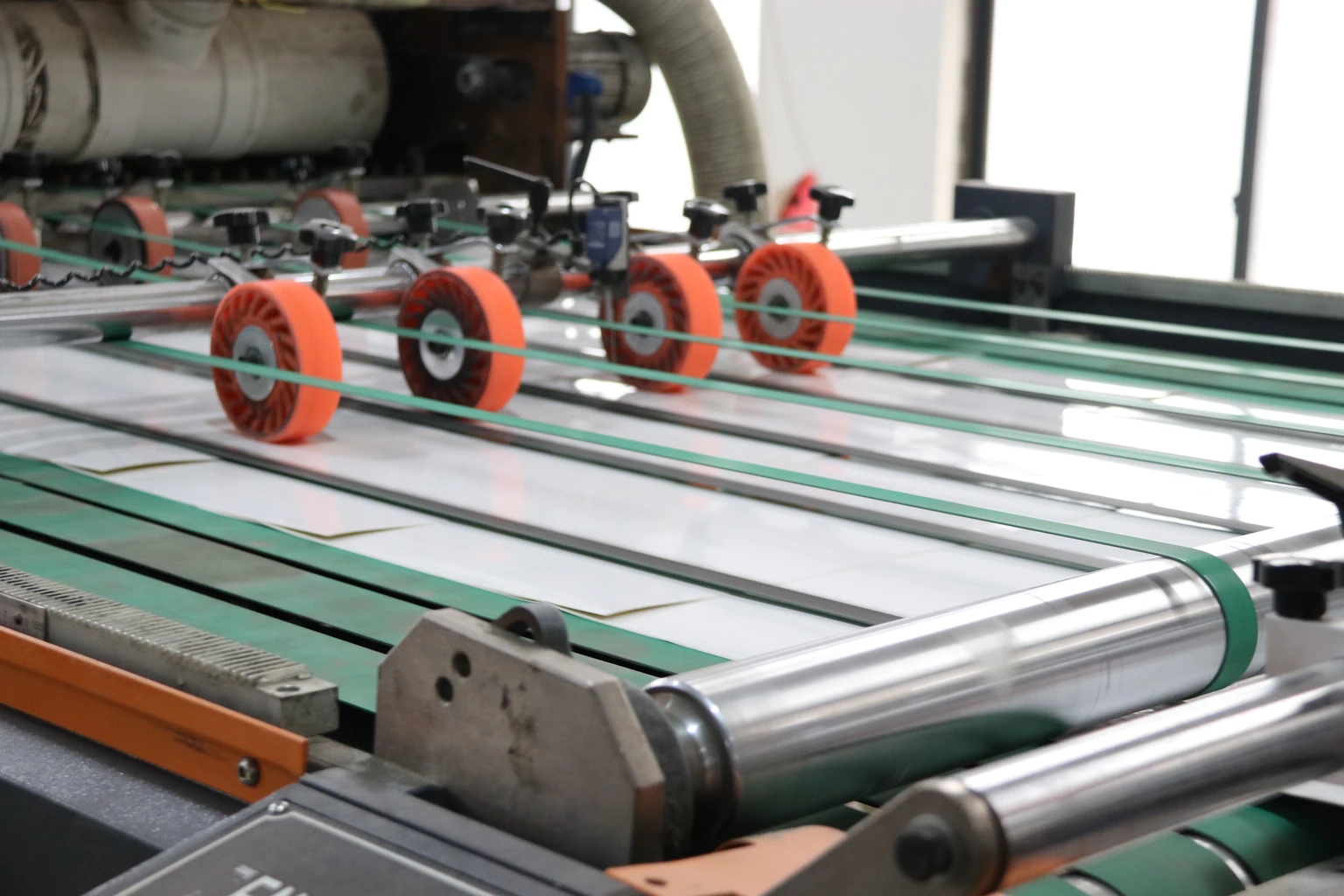 White sheets on green conveyor belts under red guide wheels