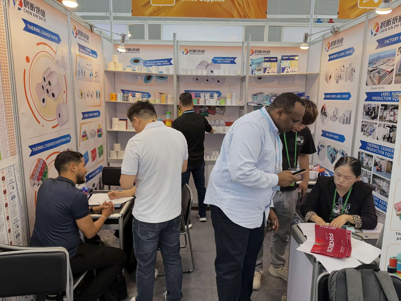 Visitors and the team talking beside displayed paper samples at the exhibition stand
