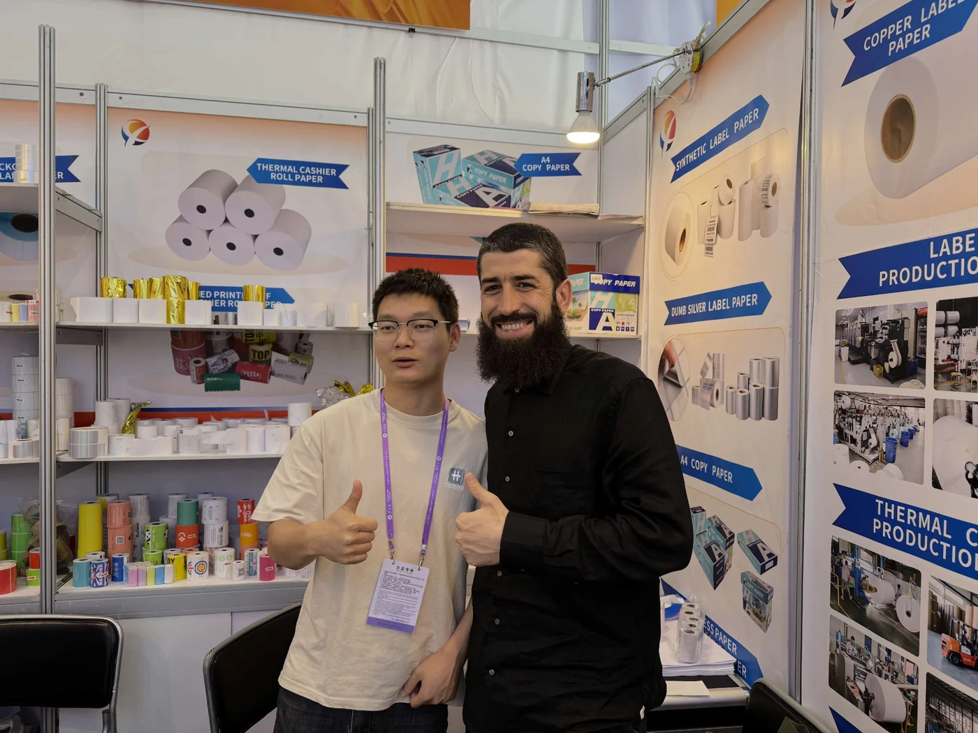 Two people beside receipt rolls and labels displayed at the exhibition stand