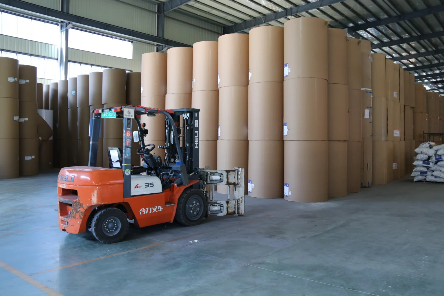 Wrapped parent paper rolls in storage beside a forklift