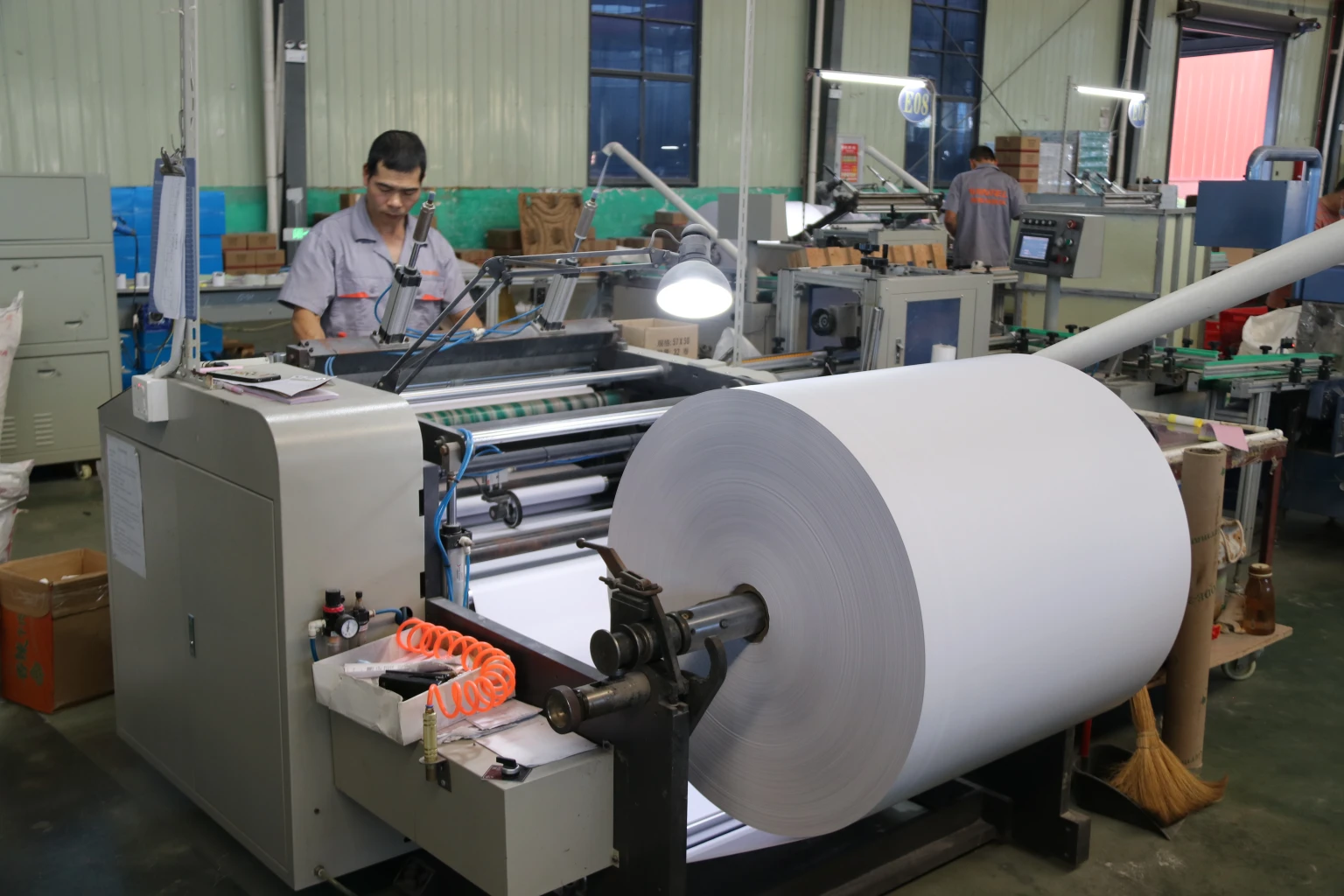 Operator and a large white paper roll on thermal-paper converting equipment